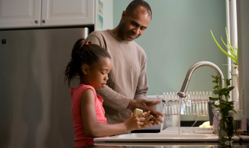 father helping daughter wash hands at the kitchen sink