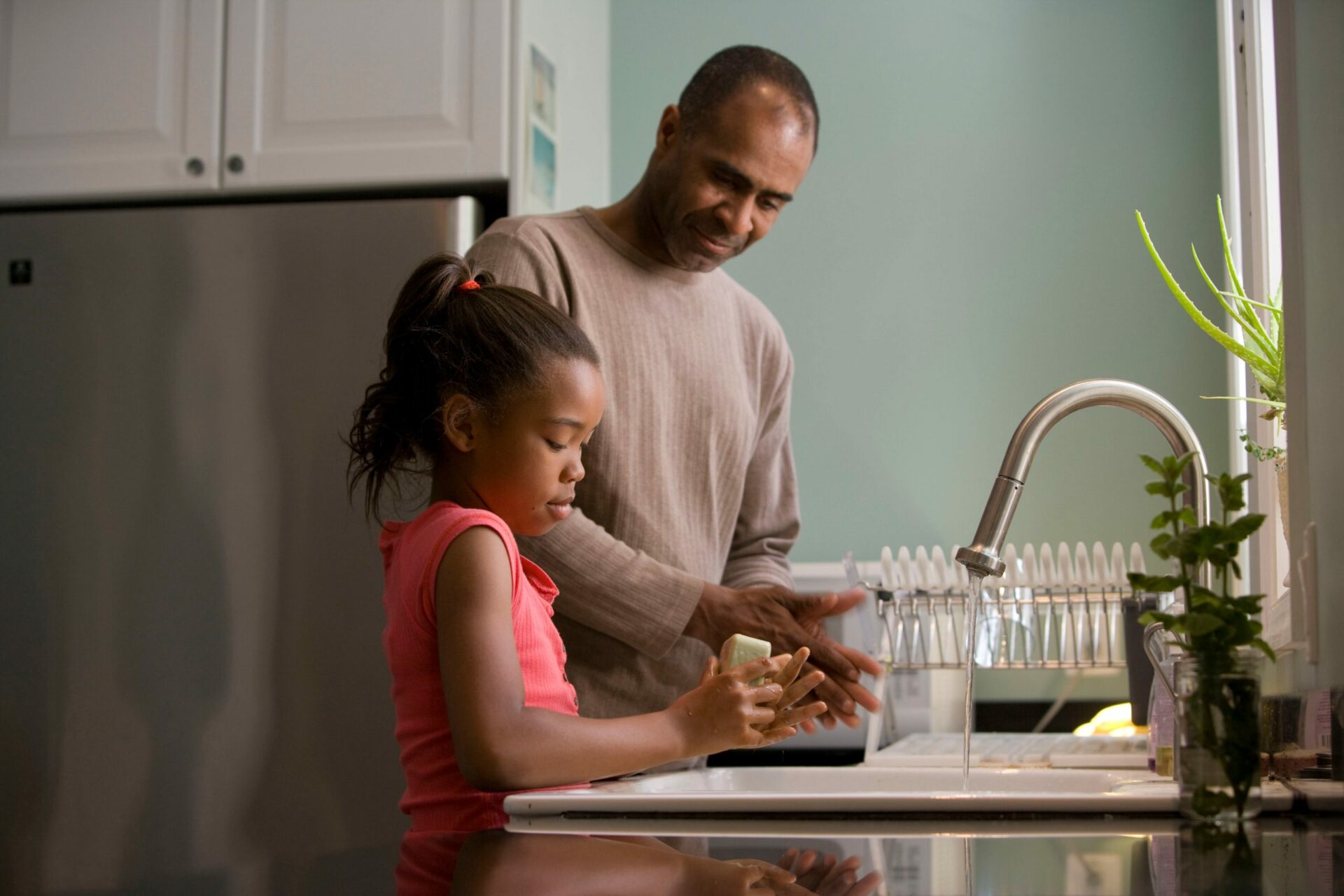 father helping daughter wash hands at the kitchen sink