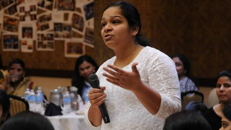 Indian mother standing with a microphone at at a parent teacher meeting